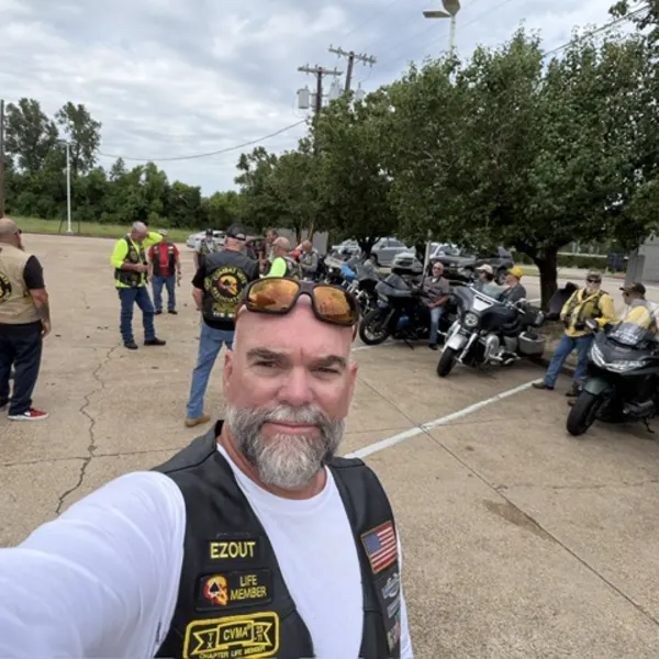 A rider in a Combat Veterans Motorcycle Association vest with motorcycles and riders assembled behind him.