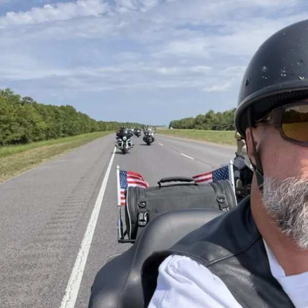 American flags mounted on the back of a motorcycle with more riders ahead on the highway.